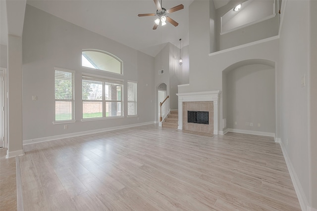 unfurnished living room featuring a tiled fireplace, high vaulted ceiling, light hardwood / wood-style floors, and ceiling fan