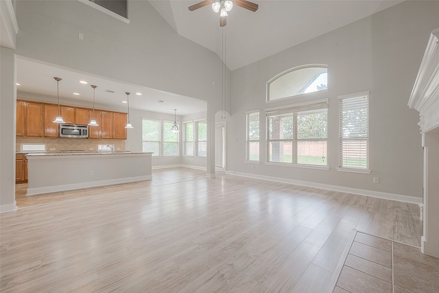 unfurnished living room with plenty of natural light, high vaulted ceiling, ceiling fan with notable chandelier, and decorative columns