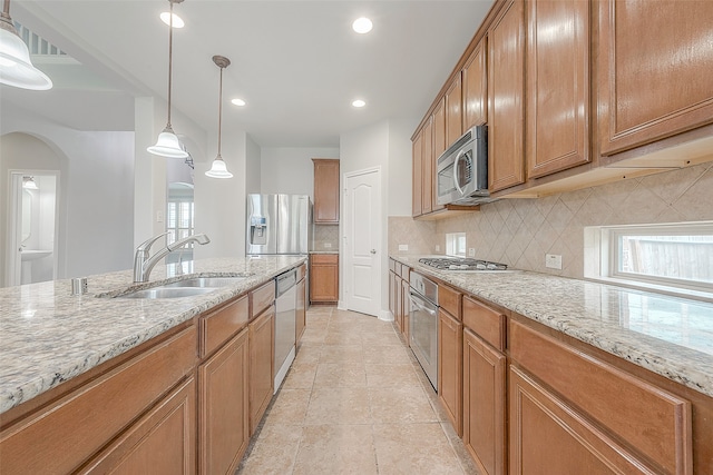 kitchen featuring light stone countertops, tasteful backsplash, appliances with stainless steel finishes, hanging light fixtures, and sink