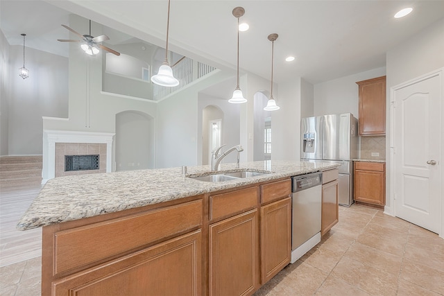 kitchen featuring an island with sink, sink, stainless steel appliances, a fireplace, and tasteful backsplash