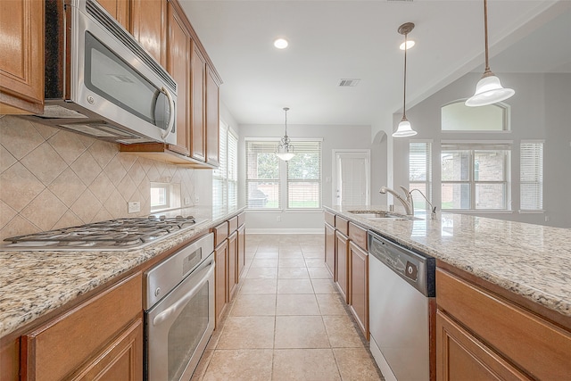 kitchen with light tile floors, light stone counters, hanging light fixtures, appliances with stainless steel finishes, and tasteful backsplash