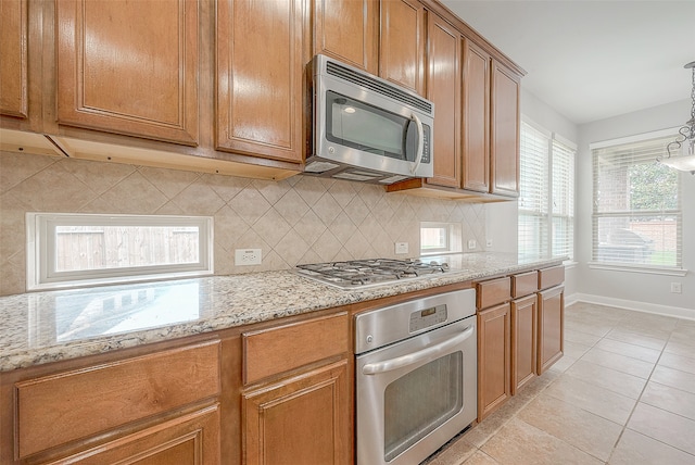 kitchen with appliances with stainless steel finishes, light stone counters, tasteful backsplash, and pendant lighting