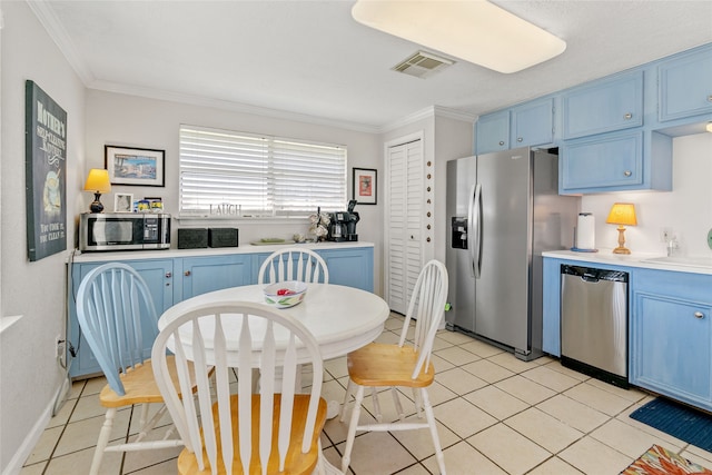 kitchen with appliances with stainless steel finishes, crown molding, blue cabinetry, and light tile floors