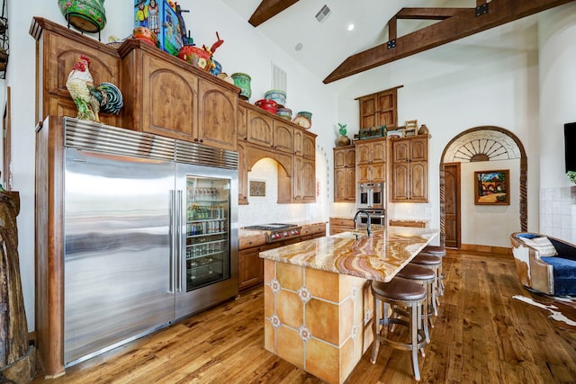 kitchen featuring high vaulted ceiling, beamed ceiling, a kitchen bar, stainless steel appliances, and a center island with sink