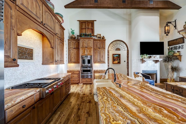 kitchen with a tiled fireplace, tasteful backsplash, dark wood-type flooring, stainless steel gas cooktop, and high vaulted ceiling