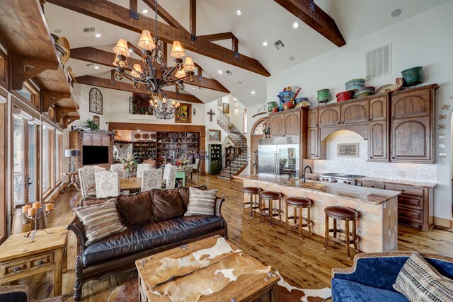 living room with high vaulted ceiling, beam ceiling, an inviting chandelier, and light hardwood / wood-style floors