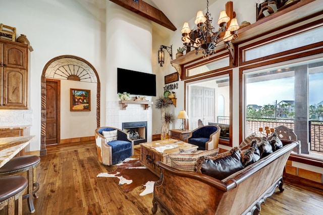 living room with high vaulted ceiling, a tiled fireplace, an inviting chandelier, and hardwood / wood-style floors