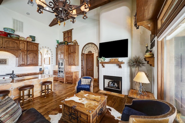 living room with sink, a towering ceiling, dark hardwood / wood-style floors, a tiled fireplace, and a chandelier