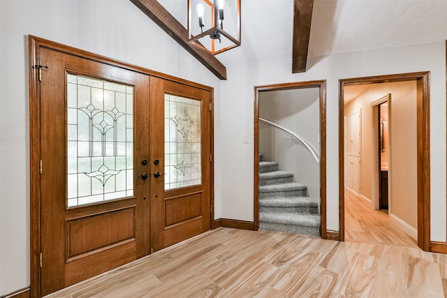 entrance foyer featuring light hardwood / wood-style flooring, french doors, a textured ceiling, and lofted ceiling with beams