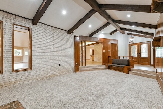 unfurnished living room with vaulted ceiling with beams, french doors, light colored carpet, and brick wall