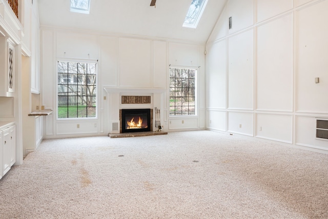 unfurnished living room featuring high vaulted ceiling, light colored carpet, ceiling fan, and a skylight