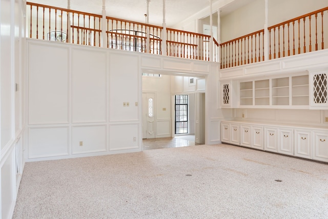 unfurnished living room featuring light colored carpet and a towering ceiling