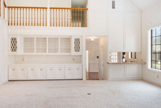 unfurnished living room with light carpet, a wealth of natural light, and a high ceiling