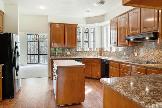 kitchen featuring light colored carpet, black appliances, tasteful backsplash, a notable chandelier, and a center island