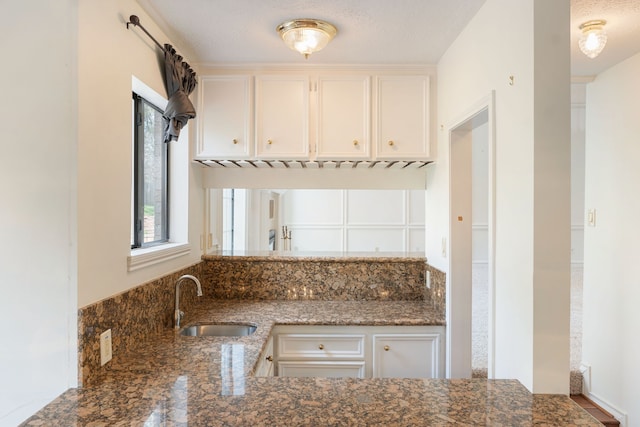 kitchen featuring white cabinetry, a textured ceiling, sink, and dark stone counters