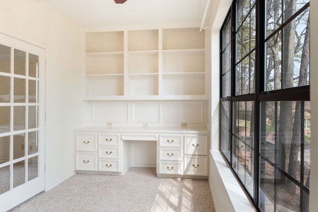 unfurnished office featuring light carpet, built in desk, and a wealth of natural light