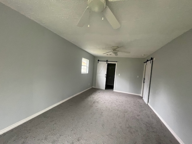 empty room featuring a textured ceiling, carpet, ceiling fan, and a barn door