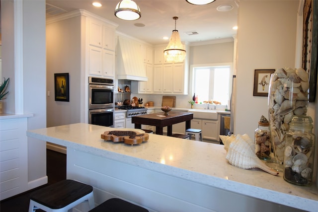 kitchen with light stone countertops, custom exhaust hood, stainless steel appliances, ornamental molding, and white cabinetry