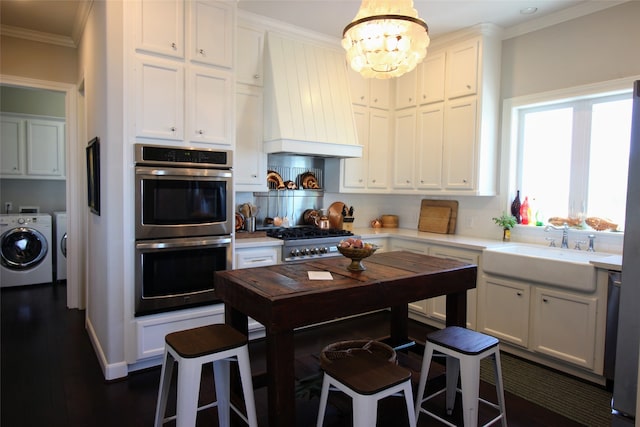 kitchen with double oven, an inviting chandelier, hanging light fixtures, washing machine and dryer, and premium range hood