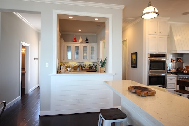 kitchen with double oven, dark hardwood / wood-style flooring, white cabinetry, ornamental molding, and a breakfast bar