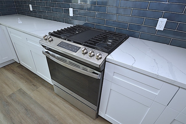 kitchen with white cabinets, light hardwood / wood-style flooring, tasteful backsplash, light stone counters, and stainless steel range with gas stovetop