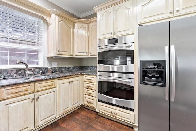 kitchen featuring sink, dark stone counters, crown molding, dark hardwood / wood-style flooring, and appliances with stainless steel finishes