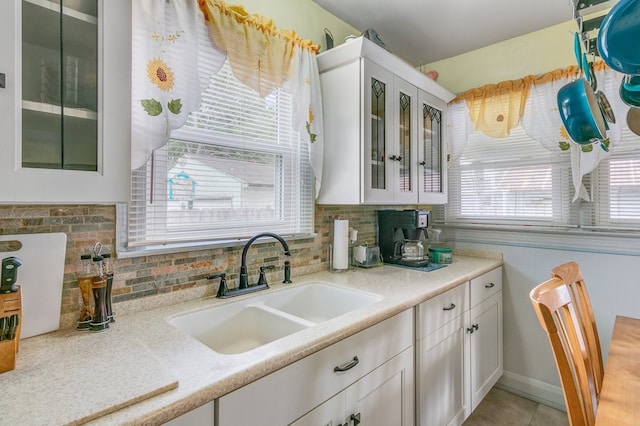 kitchen with sink, white cabinets, light tile floors, and backsplash