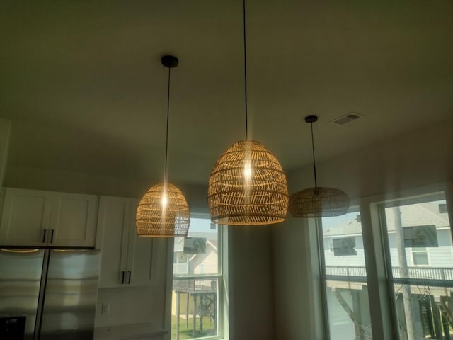 interior details featuring white cabinetry, stainless steel refrigerator, and decorative light fixtures