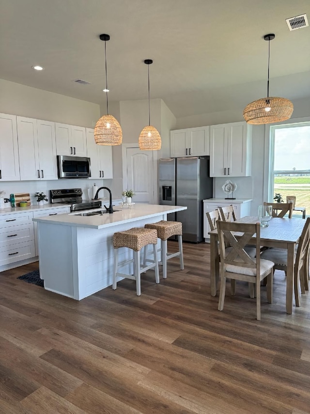 kitchen with white cabinets, stainless steel appliances, decorative light fixtures, and dark wood-type flooring