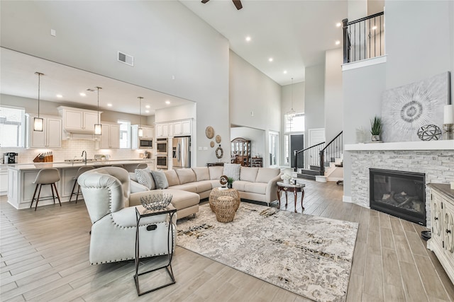 living room with ceiling fan, light hardwood / wood-style flooring, a fireplace, sink, and a high ceiling