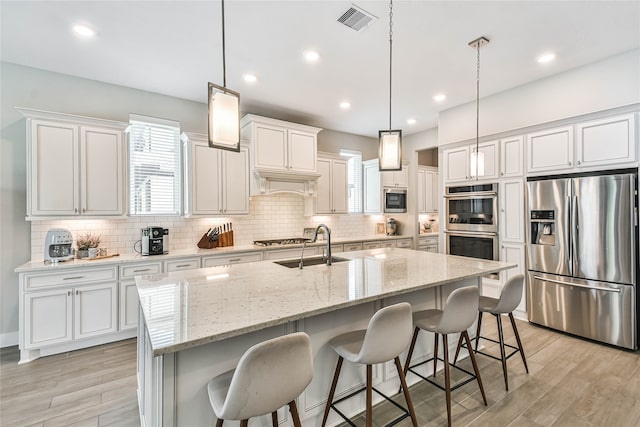 kitchen featuring pendant lighting, stainless steel appliances, white cabinetry, and a center island with sink