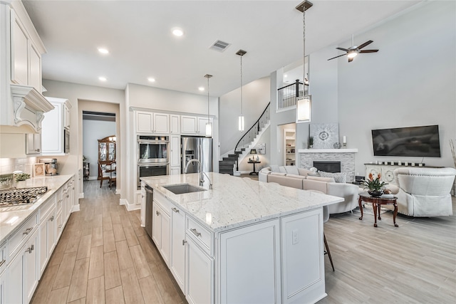 kitchen with ceiling fan, white cabinetry, appliances with stainless steel finishes, and a stone fireplace