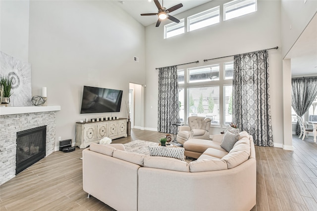 living room featuring a fireplace, a high ceiling, light hardwood / wood-style floors, and ceiling fan