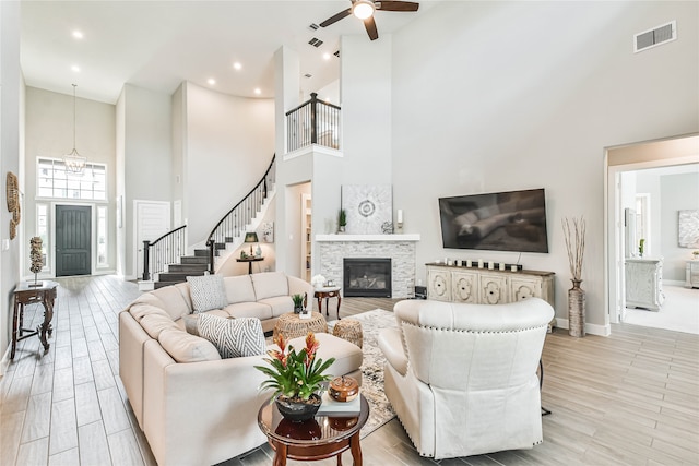 living room with a high ceiling, a stone fireplace, and ceiling fan with notable chandelier