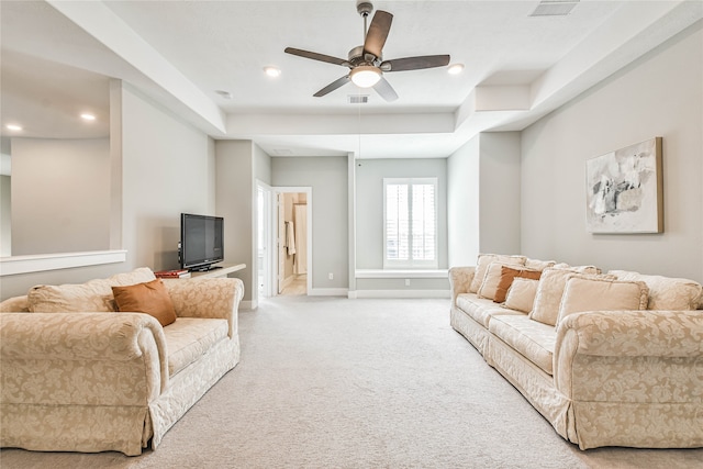 carpeted living room with a raised ceiling and ceiling fan