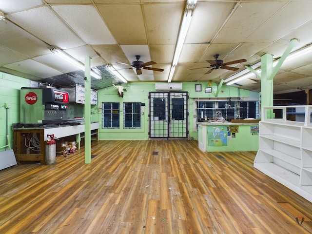 interior space with ceiling fan, a drop ceiling, dark hardwood / wood-style floors, and a wall unit AC