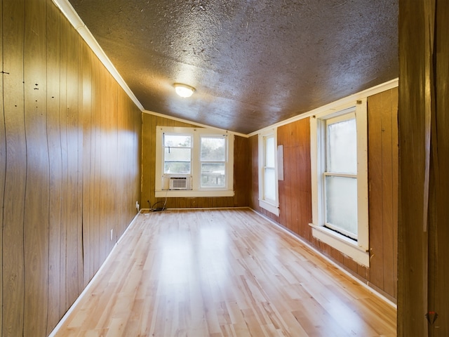 empty room featuring wooden walls, vaulted ceiling, a textured ceiling, light hardwood / wood-style flooring, and ornamental molding