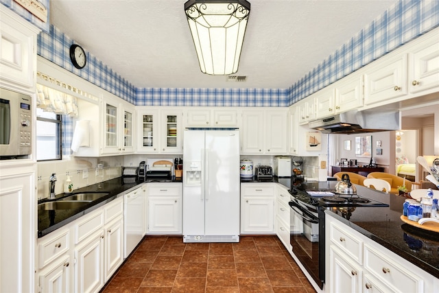 kitchen featuring dark stone countertops, white appliances, sink, white cabinetry, and a textured ceiling