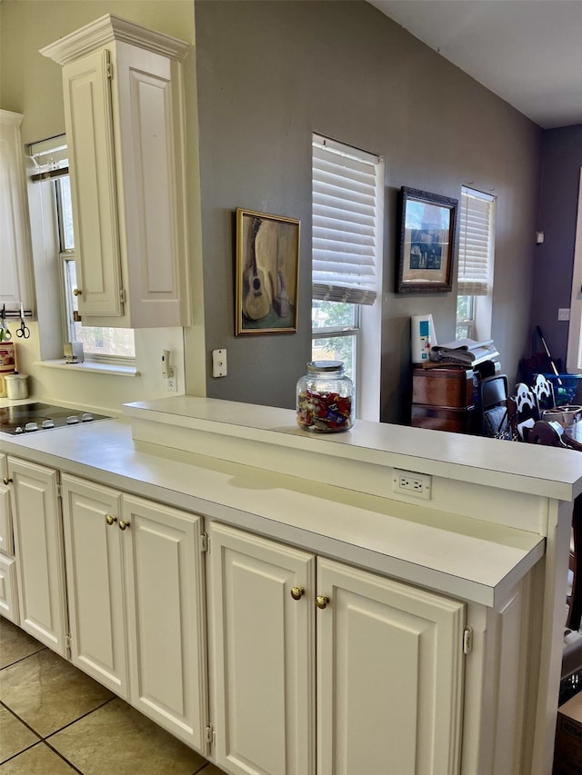 kitchen with white cabinets, electric stovetop, light tile flooring, and kitchen peninsula