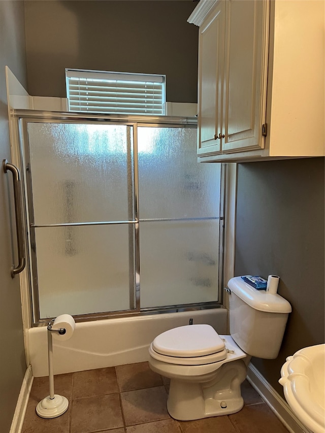 bathroom featuring toilet, bath / shower combo with glass door, and tile flooring