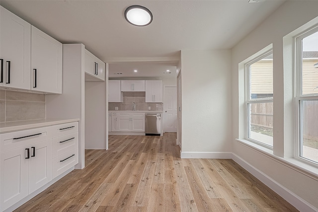 kitchen with backsplash, light hardwood / wood-style floors, white cabinets, and stainless steel dishwasher