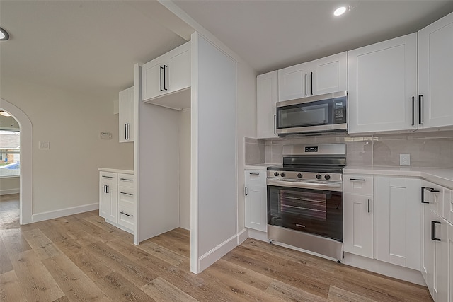 kitchen with white cabinets, backsplash, light hardwood / wood-style floors, and stainless steel appliances