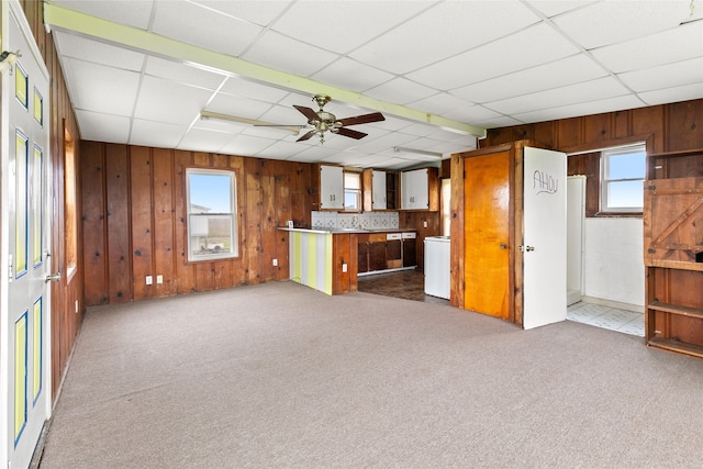 unfurnished living room with wood walls, ceiling fan, dark carpet, and a paneled ceiling