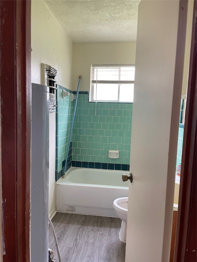 bathroom featuring tiled shower / bath combo, toilet, hardwood / wood-style flooring, and a textured ceiling