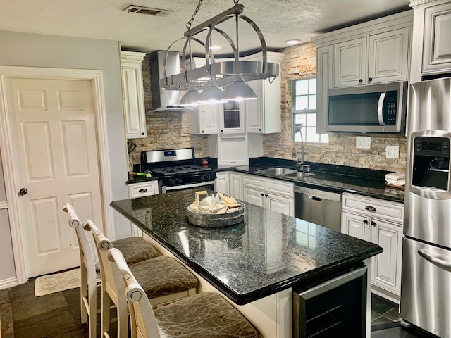 kitchen featuring stainless steel appliances, a kitchen island, an inviting chandelier, tasteful backsplash, and sink