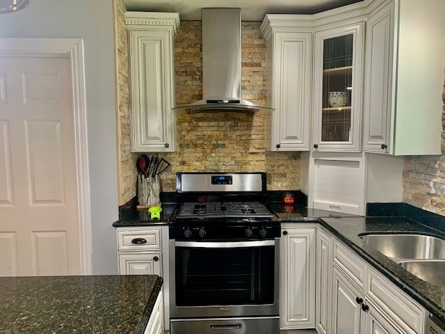 kitchen with dark stone counters, stainless steel range with gas cooktop, white cabinetry, and wall chimney range hood