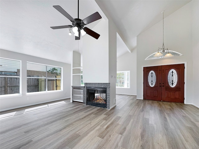 entrance foyer featuring ceiling fan with notable chandelier, light hardwood / wood-style floors, a tile fireplace, and high vaulted ceiling