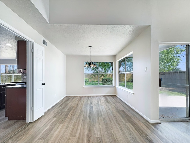 unfurnished dining area with a textured ceiling, a chandelier, and light hardwood / wood-style floors