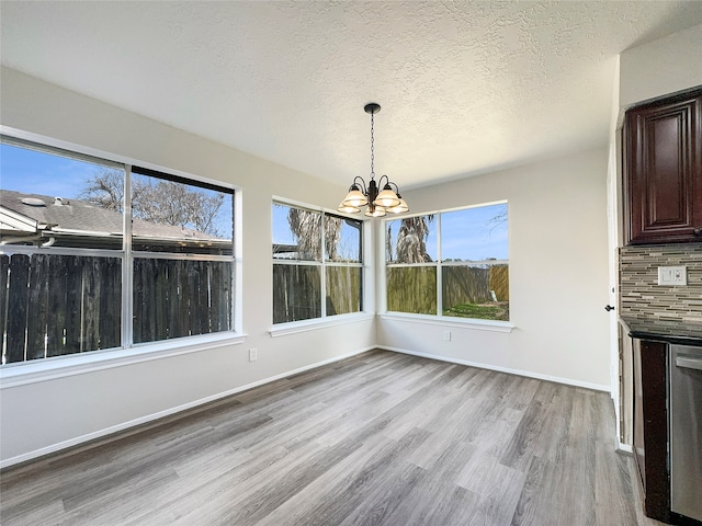 unfurnished dining area featuring plenty of natural light, a textured ceiling, a notable chandelier, and hardwood / wood-style flooring