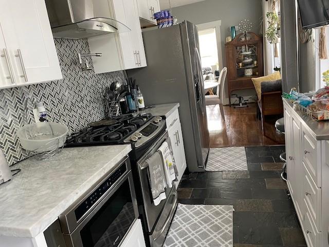 kitchen featuring appliances with stainless steel finishes, a healthy amount of sunlight, white cabinets, and exhaust hood